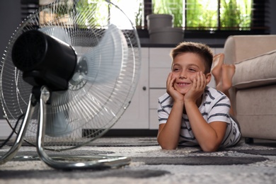 Little boy enjoying air flow from fan at home. Summer heat
