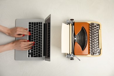 Woman working with laptop near old typewriter at light table, top view. Concept of technology progress