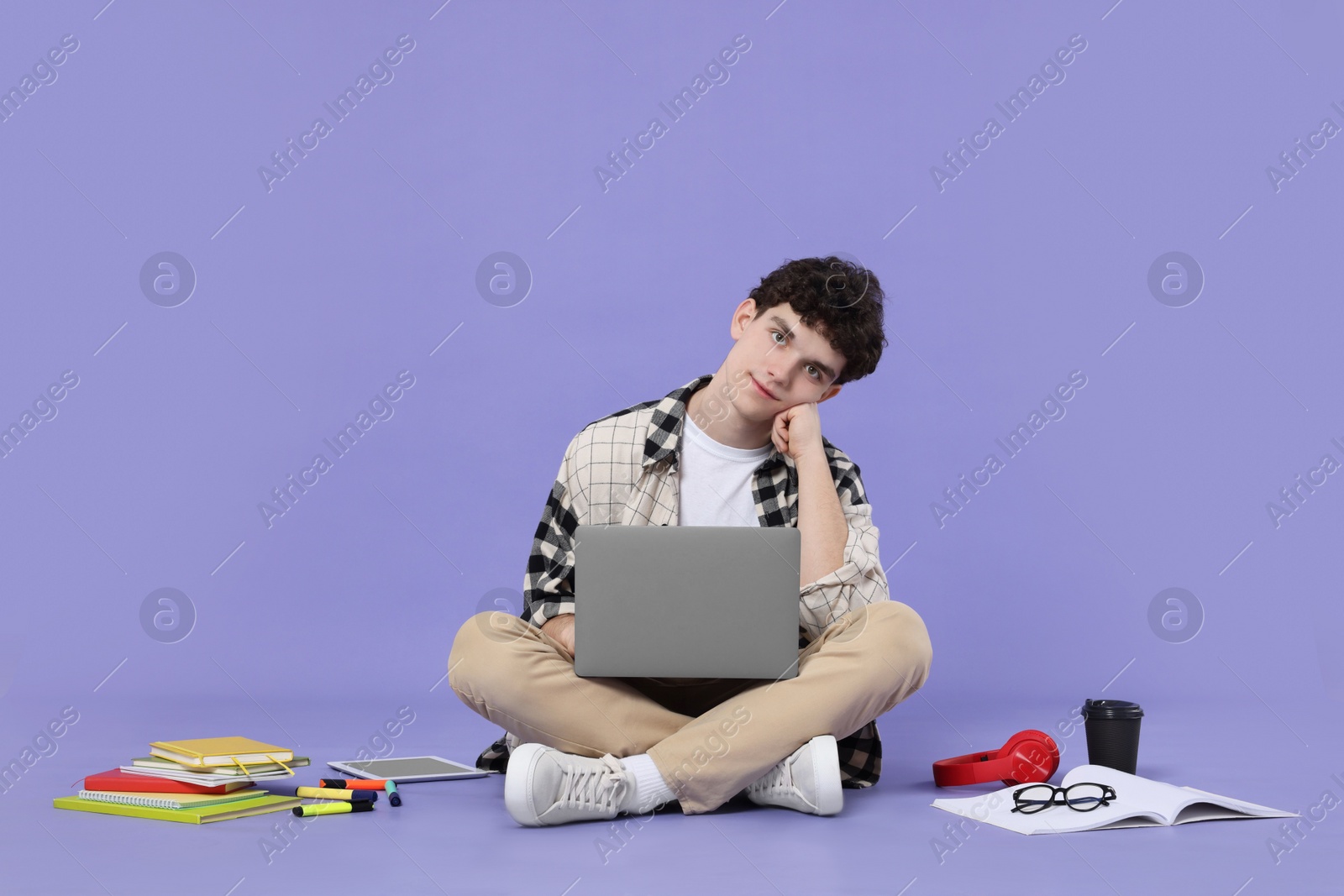 Photo of Portrait of student with laptop and stationery sitting on purple background