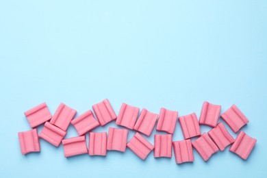 Photo of Tasty pink chewing gums on light blue background, flat lay. Space for text