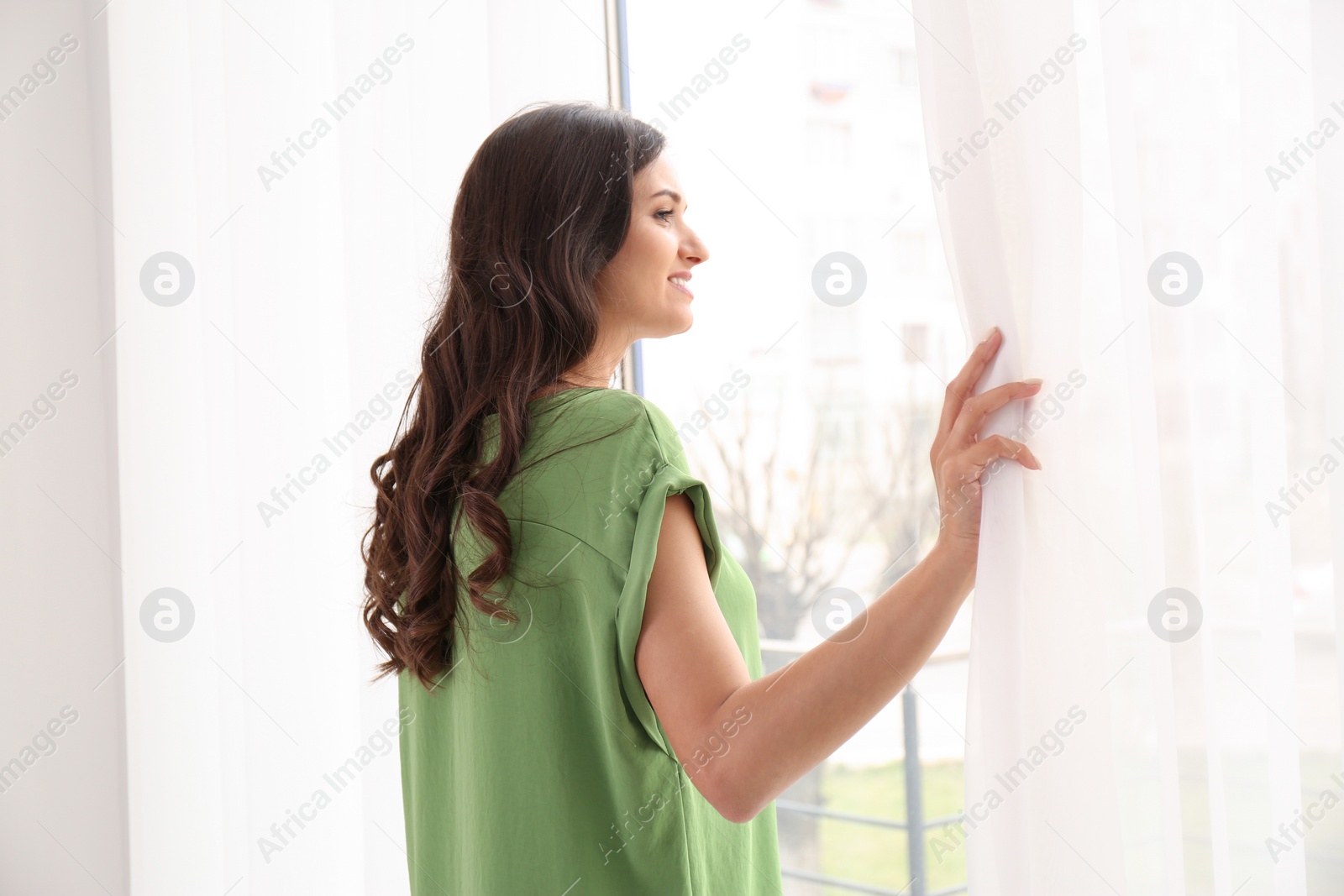 Photo of Beautiful young woman looking out of window at home