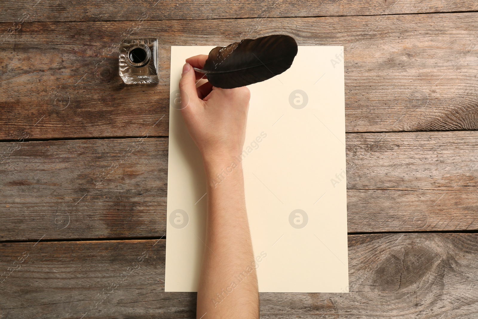 Photo of Woman using feather pen to write with ink on parchment at wooden table, top view. Space for text
