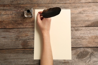 Woman using feather pen to write with ink on parchment at wooden table, top view. Space for text