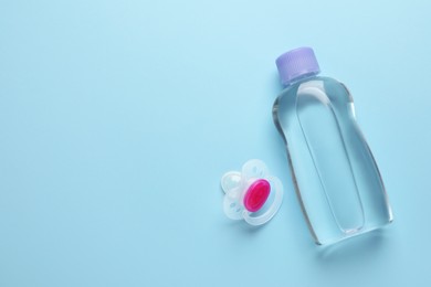 Photo of Bottle of baby oil and pacifier on light blue background, flat lay. Space for text