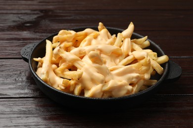 Delicious french fries with cheese sauce in bowl on wooden table, closeup