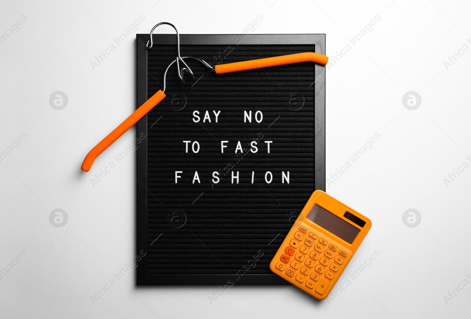 Photo of Black letter board with phrase SAY NO TO FAST FASHION, orange hanger and calculator on white background, top view