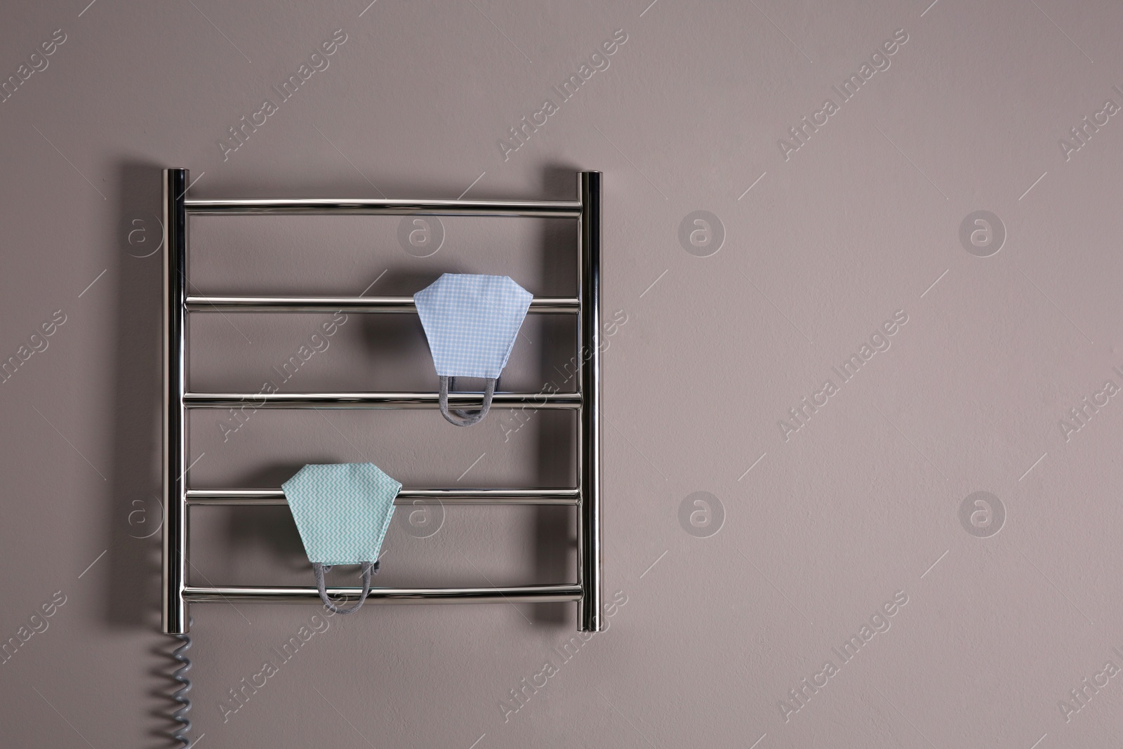 Photo of Modern heated towel rail with cloth face masks on grey wall. Space for text