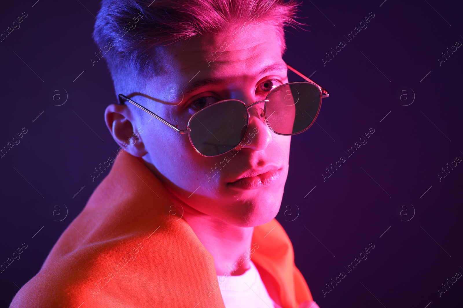 Photo of Stylish young man in sunglasses on dark background in neon lights