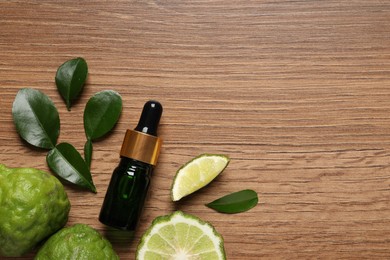 Glass bottle of bergamot essential oil and fresh fruits on wooden table, flat lay. Space for text