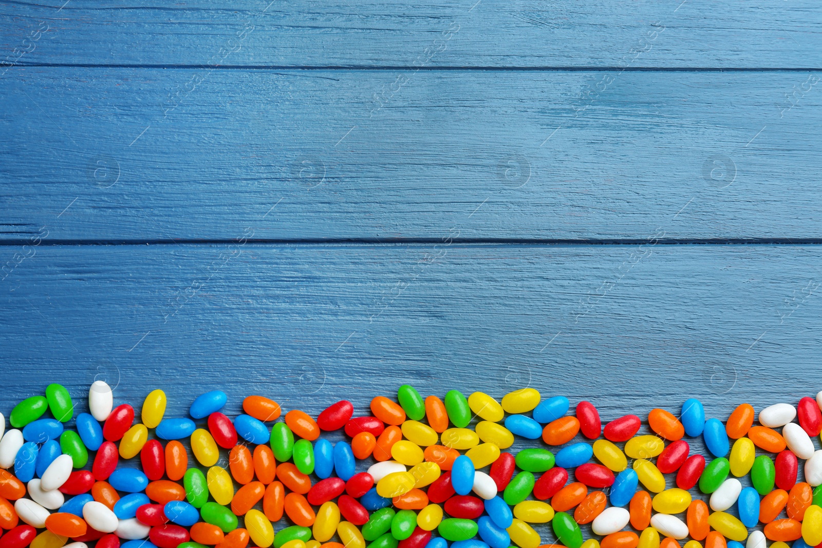 Photo of Colorful jelly beans on blue wooden background, flat lay. Space for text