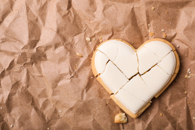 Photo of Broken heart shaped cookie on crumpled paper, top view with space for text. Relationship problems concept