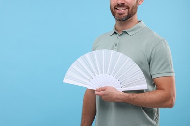 Photo of Man holding hand fan on light blue background, closeup. Space for text