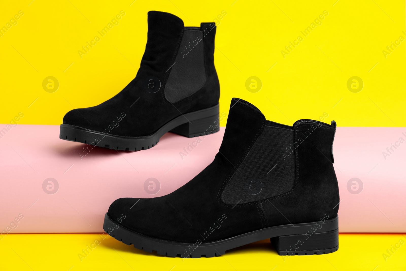 Photo of Stylish black female boots on yellow background