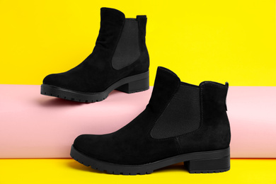 Stylish black female boots on yellow background