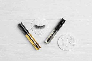 False eyelashes and tubes of different oils on white wooden table, flat lay