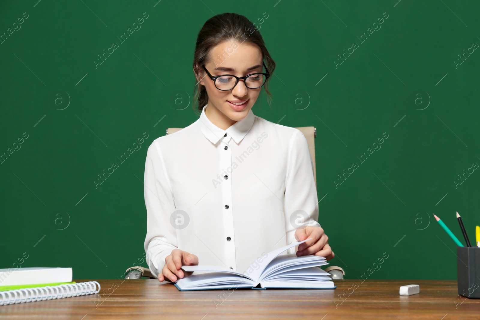 Photo of Portrait of beautiful young teacher sitting at table near chalkboard