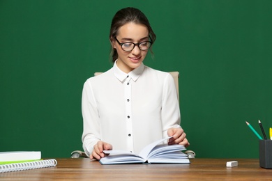 Portrait of beautiful young teacher sitting at table near chalkboard