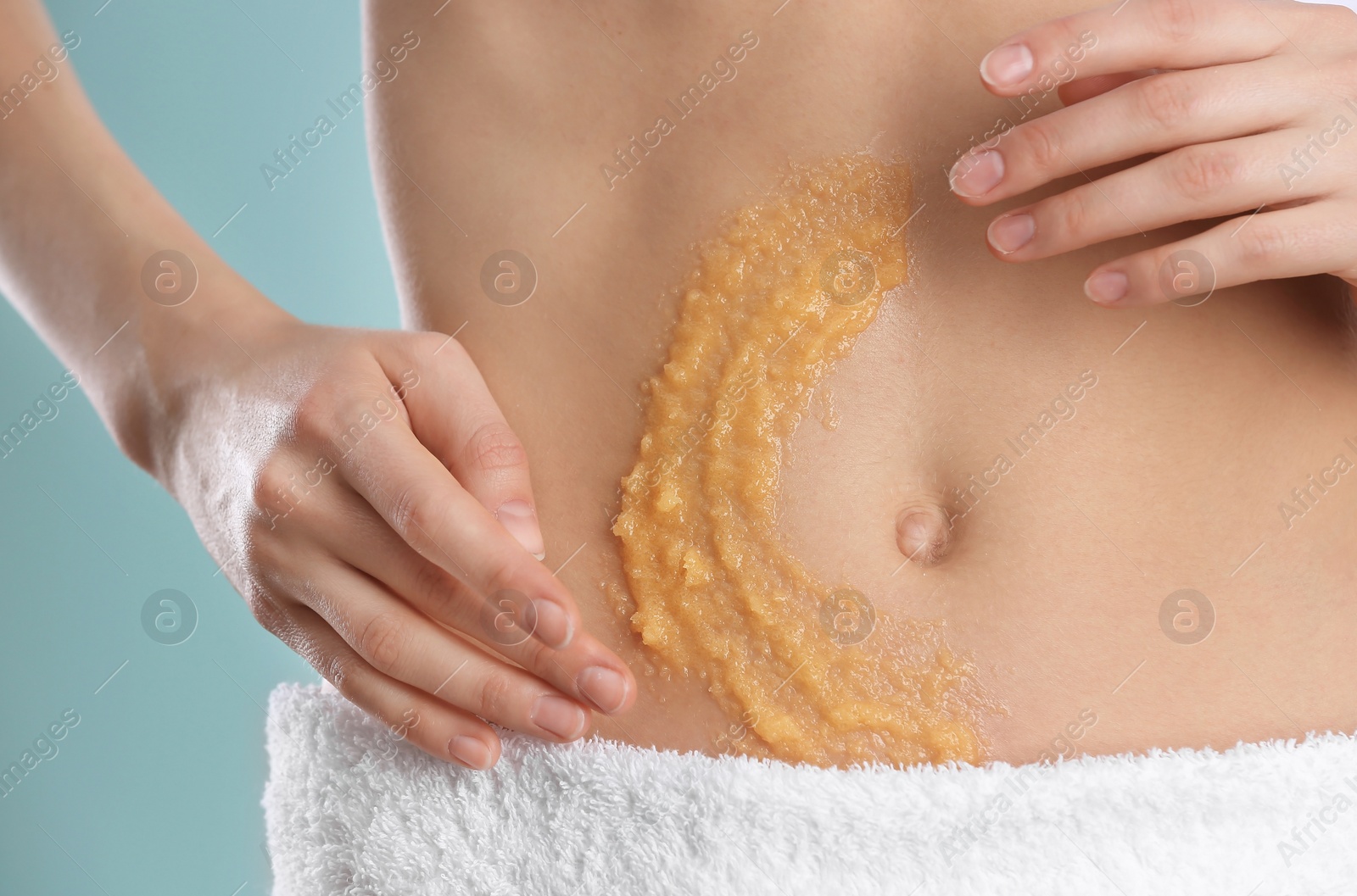 Photo of Young woman applying natural scrub on her belly against color background, closeup