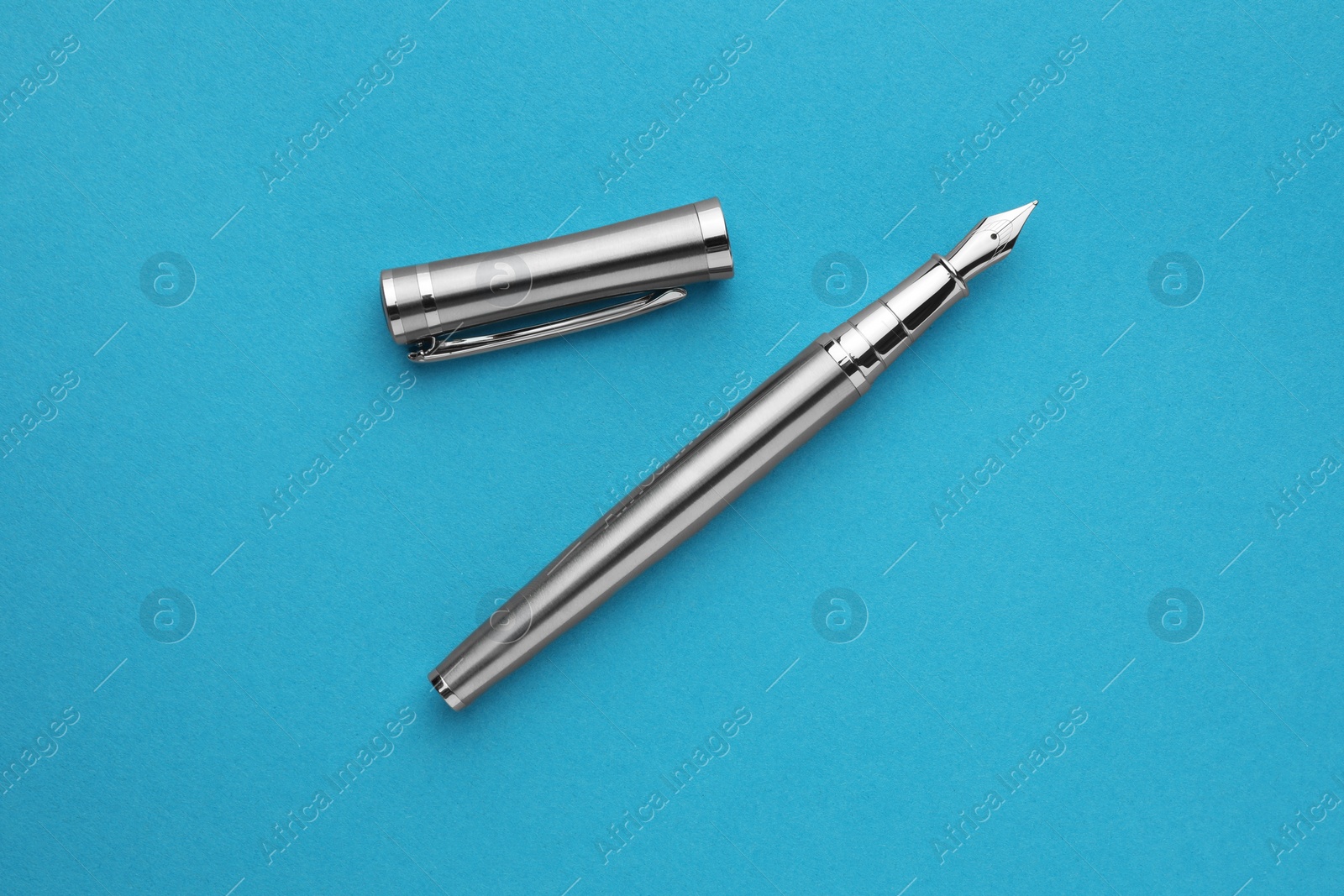 Photo of Stylish silver fountain pen with cap on light blue background, flat lay