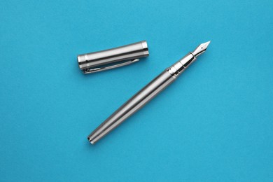 Photo of Stylish silver fountain pen with cap on light blue background, flat lay