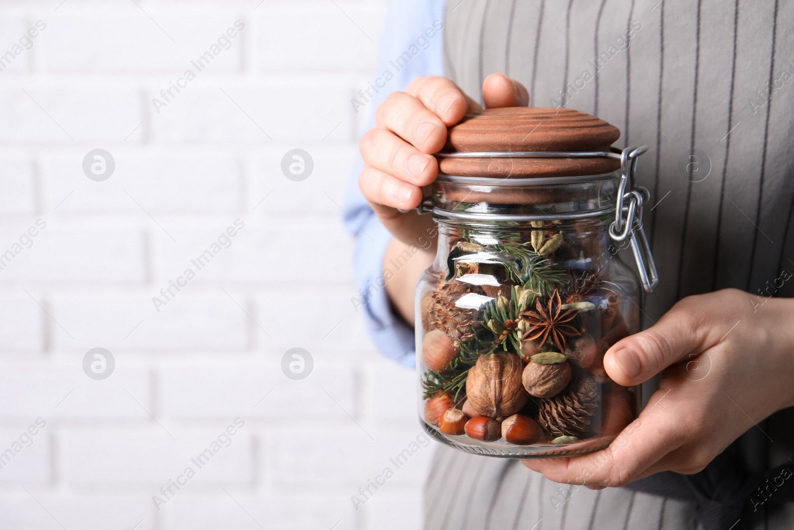 Photo of Woman holding jar with aromatic potpourri near white brick wall, closeup. Space for text
