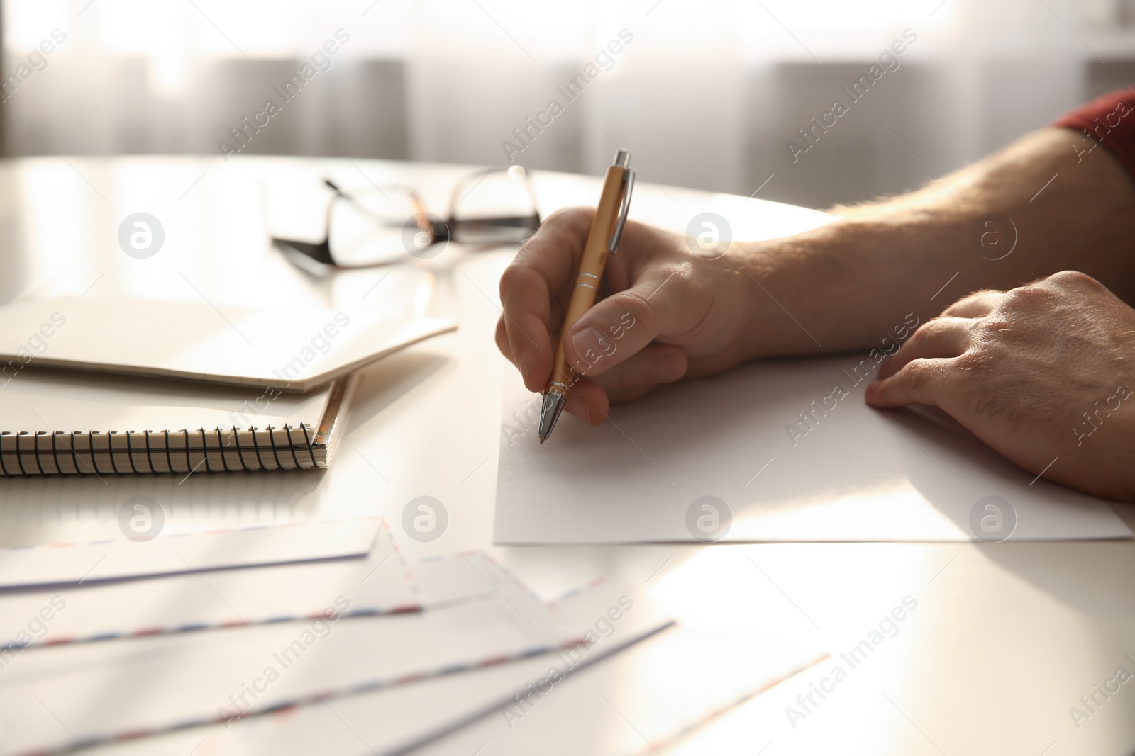 Photo of Man writing letter at white table in room, closeup