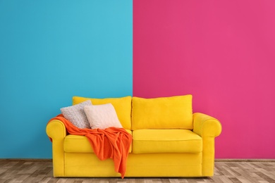 Photo of Sofa with different pillows near color wall in room