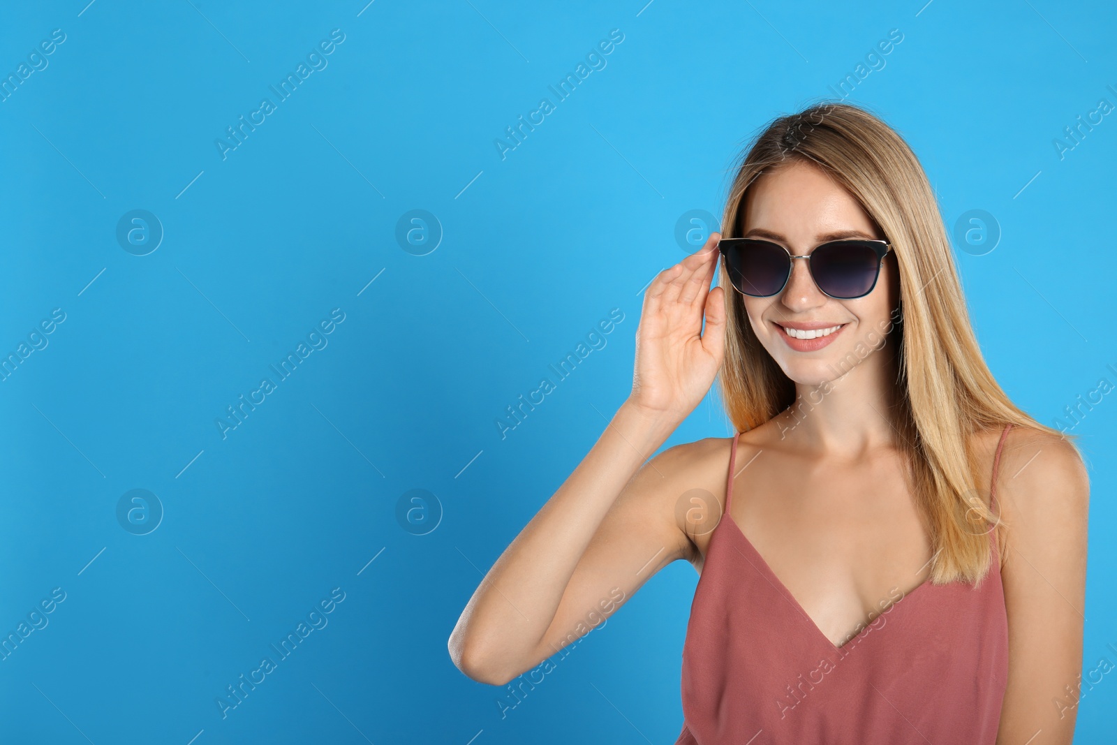 Photo of Beautiful woman in stylish sunglasses on light blue background, space for text