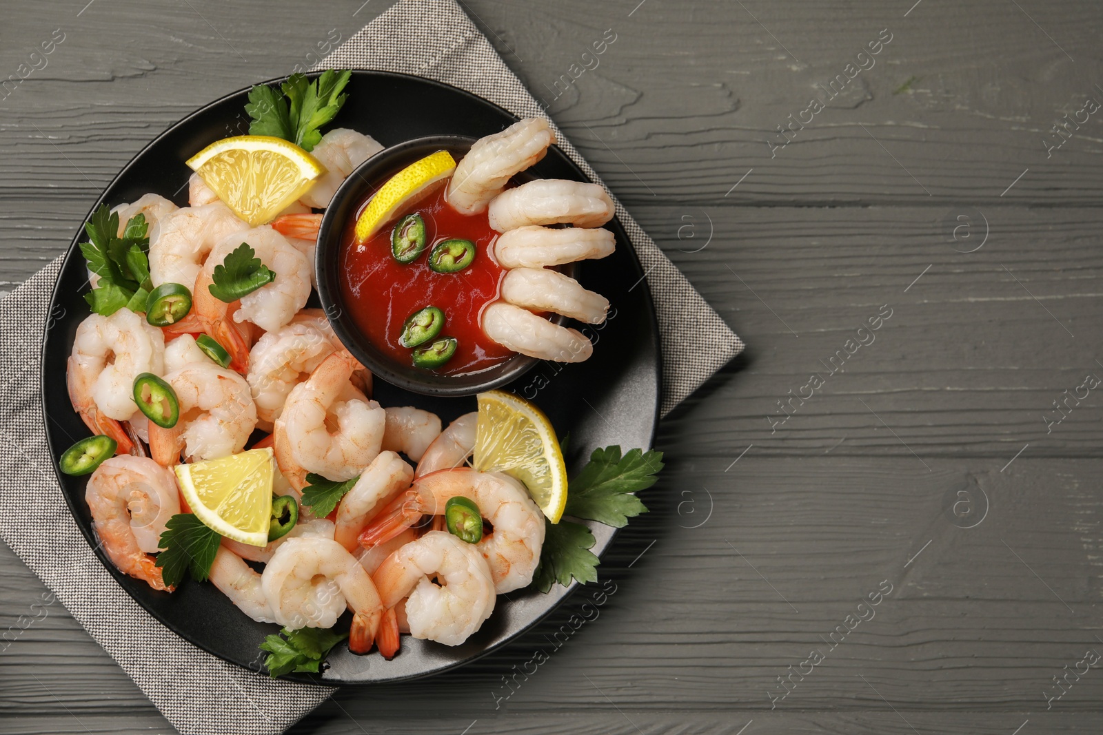 Photo of Tasty boiled shrimps with cocktail sauce, chili, parsley and lemon on grey wooden table, top view. Space for text