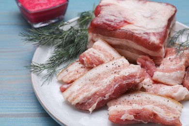 Pieces of pork fatback with dill and sauce on light blue wooden table, closeup