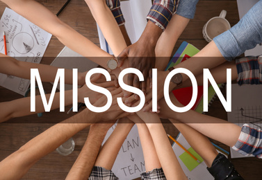 People holding hands over wooden table and text MISSION, top view