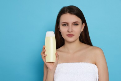 Photo of Beautiful young woman wrapped in towel holding bottle of shampoo on light blue background. Space for text