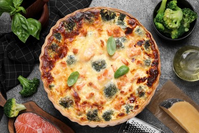 Delicious homemade quiche and ingredients on gray table, flat lay