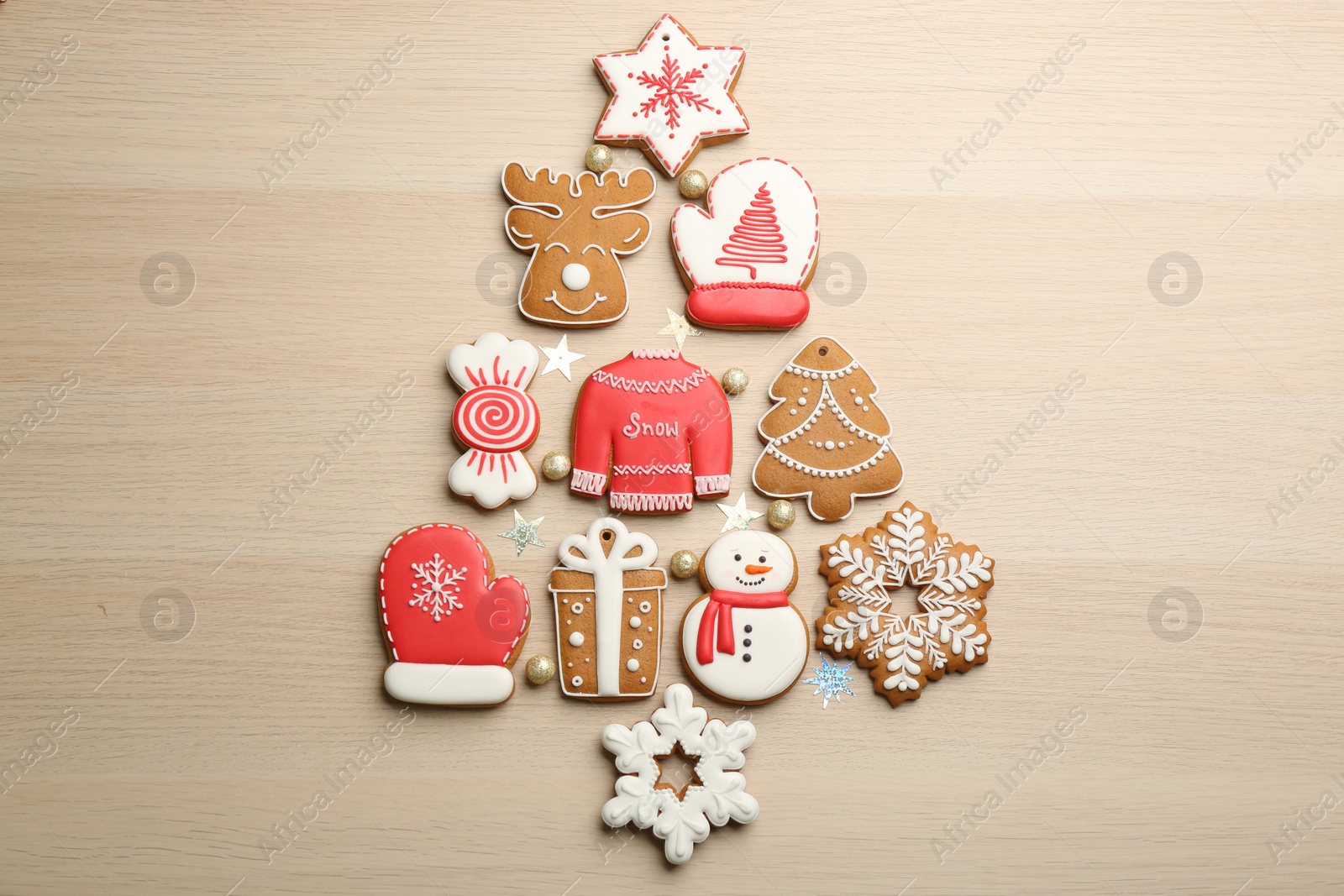 Photo of Christmas tree shape made of delicious decorated gingerbread cookies on wooden table, flat lay