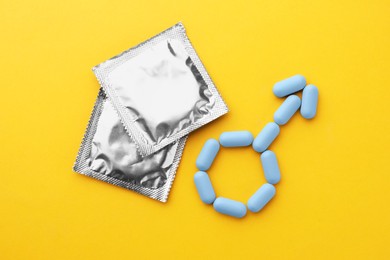 Photo of Male sign made of pills and condoms on orange background, flat lay. Potency problem