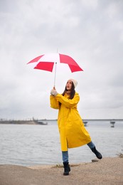 Woman in yellow raincoat with umbrella caught in gust of wind near river