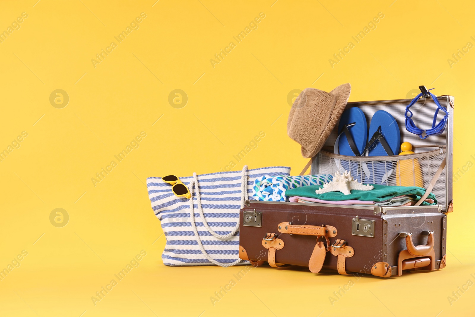 Photo of Bag and packed vintage suitcase with different beach objects on orange background, space for text. Summer vacation