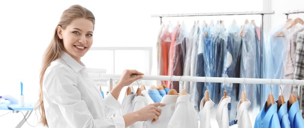 Image of Young woman near rack with clean clothes, banner design. Dry-cleaning service