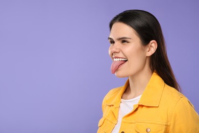 Photo of Happy young woman showing her tongue on purple background. Space for text