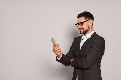 Handsome man in suit looking at smartphone on light grey background. Space for text
