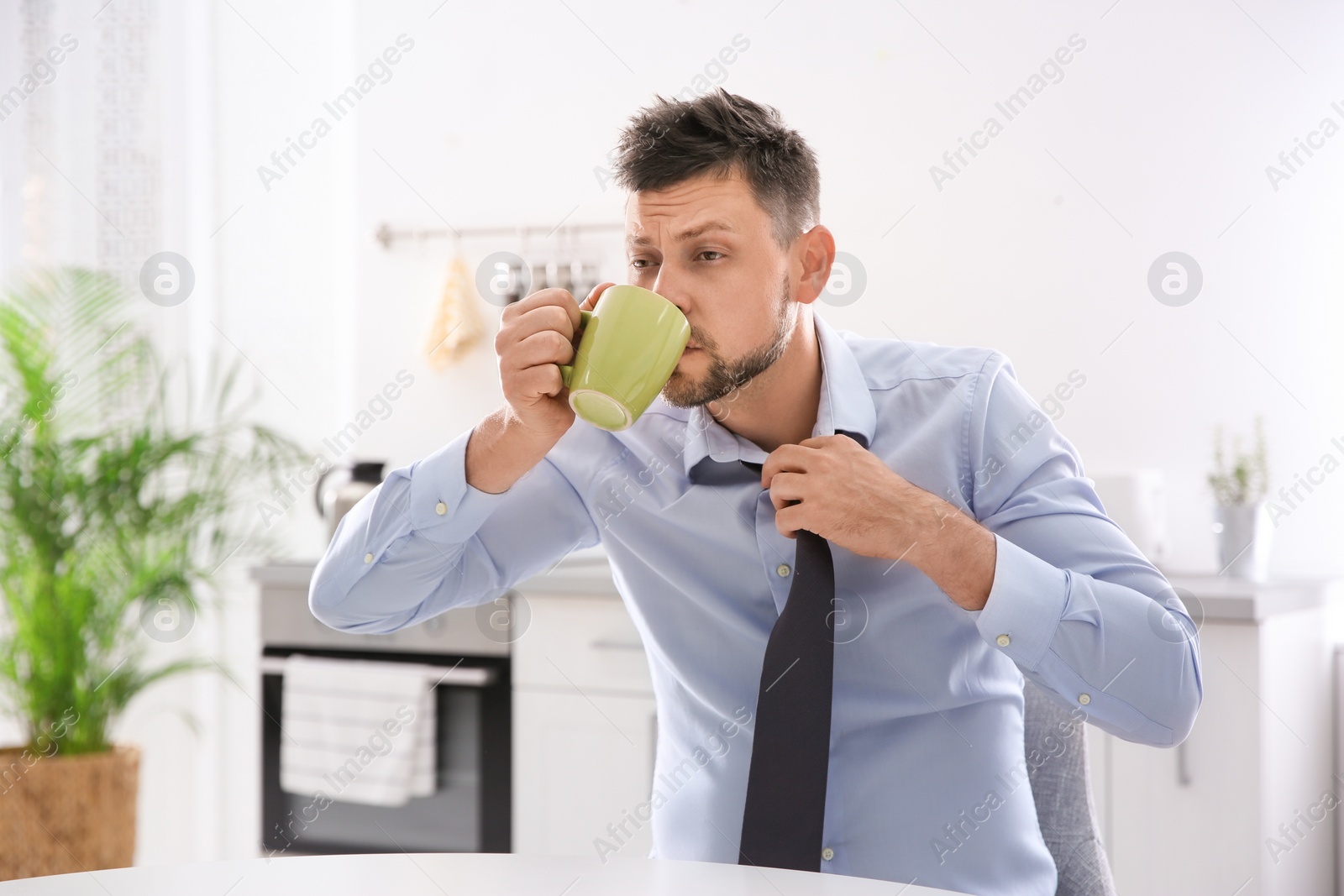 Photo of Sleepy man with cup of drink at home in morning