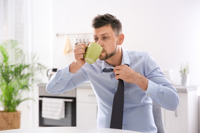 Sleepy man with cup of drink at home in morning