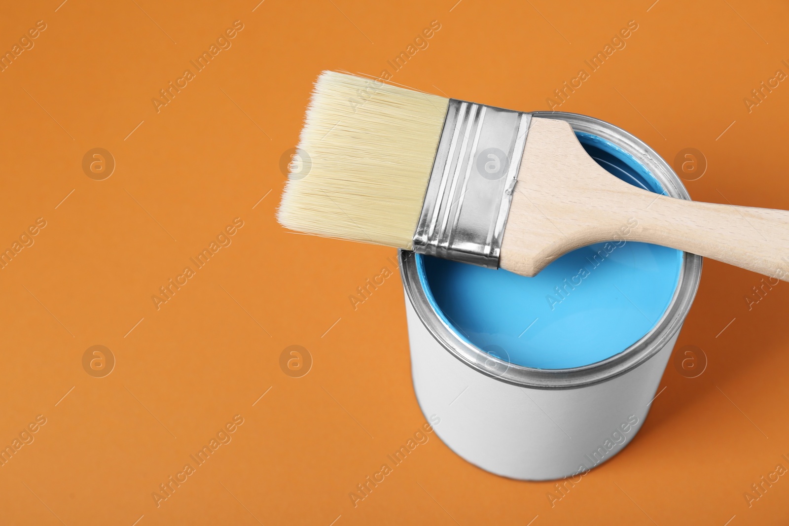 Photo of Can of light blue paint with brush on pale orange background, above view. Space for text