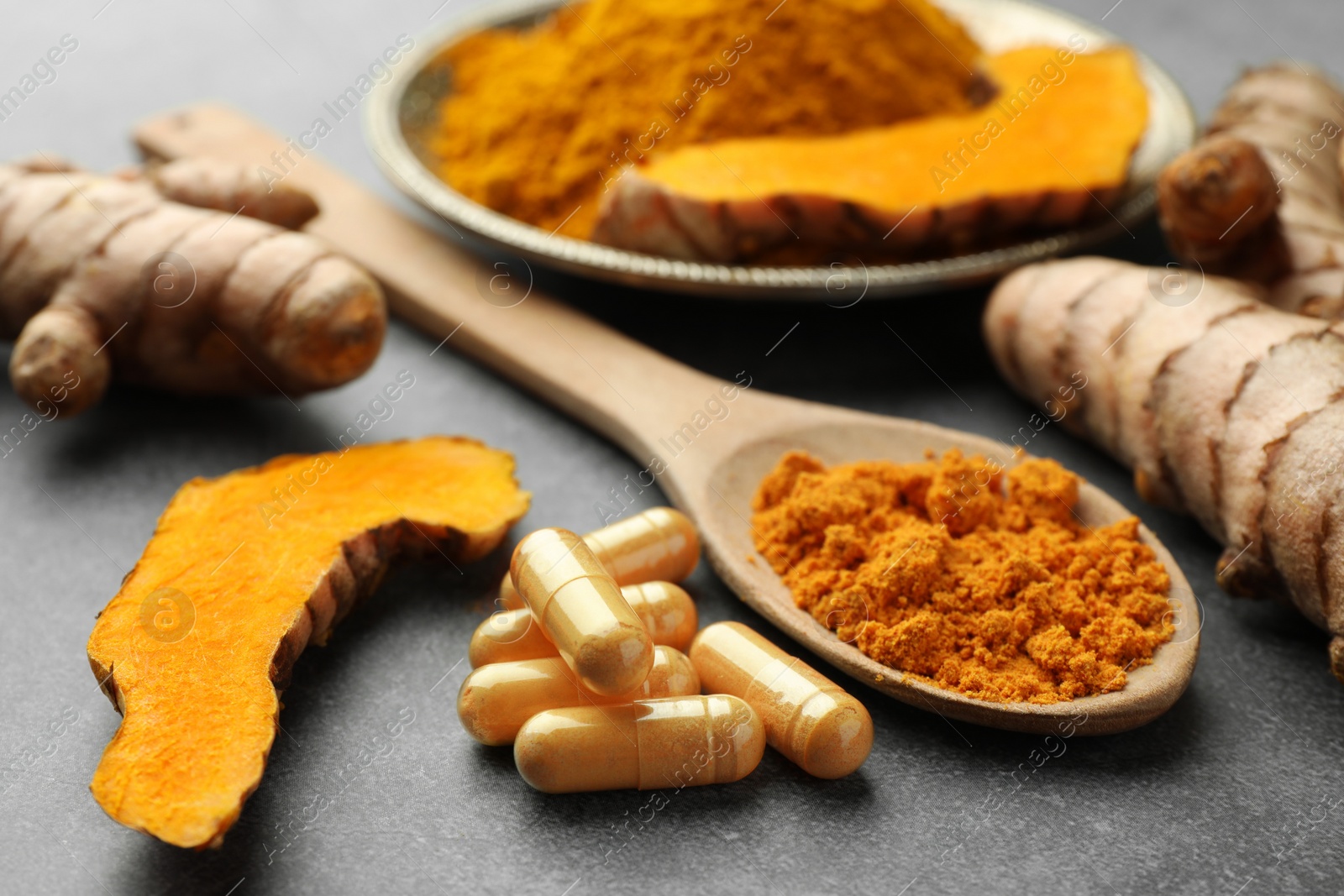 Photo of Aromatic turmeric powder, pills and raw roots on grey table, closeup