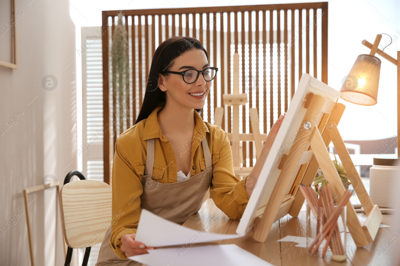 Photo of Young woman drawing on easel at table indoors