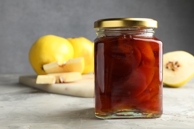 Tasty homemade quince jam in jar and fruits on grey textured table, closeup. Space for text