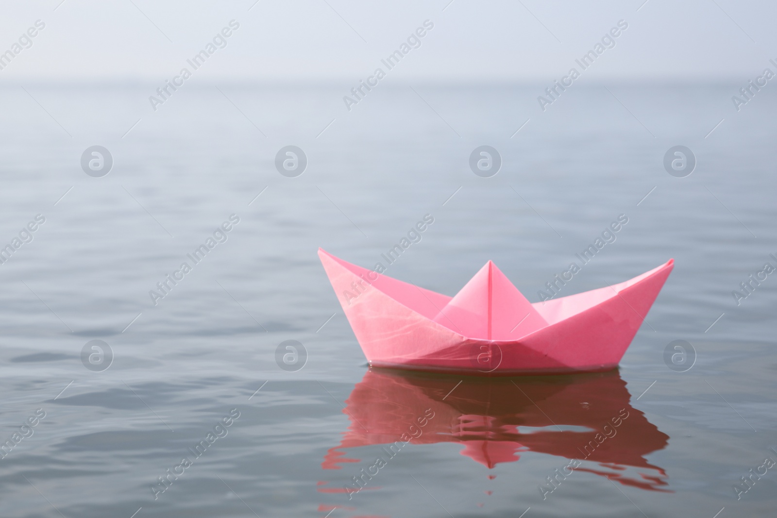 Photo of Pink paper boat on water surface, space for text