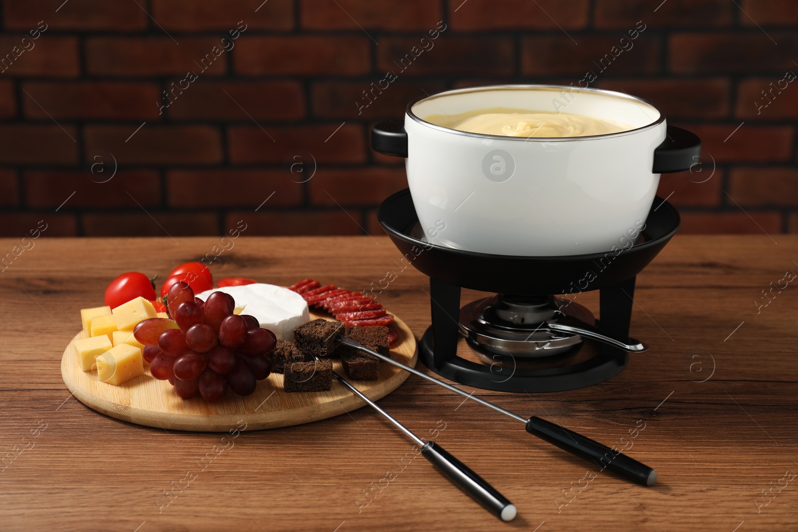 Photo of Fondue with tasty melted cheese, forks and different snacks on wooden table