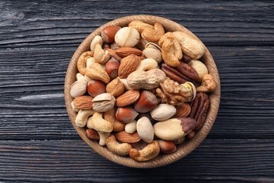 Photo of Bowl with organic mixed nuts on wooden background, top view