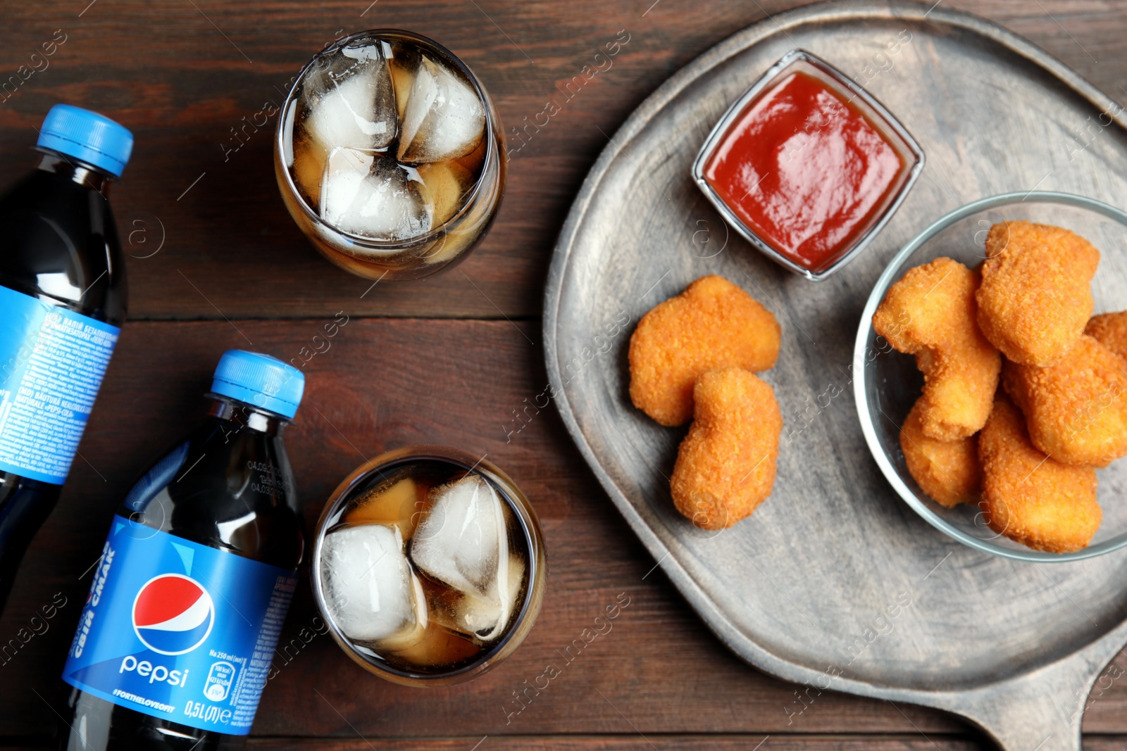 Photo of MYKOLAIV, UKRAINE - FEBRUARY 15, 2021: Glasses and bottles of Pepsi with snack on wooden table, flat lay